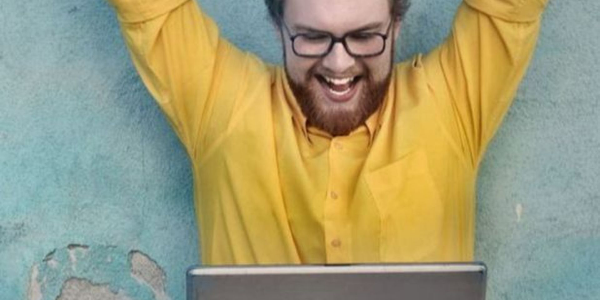 man sitting cross legged with laptop and arms triumphantly in the air 