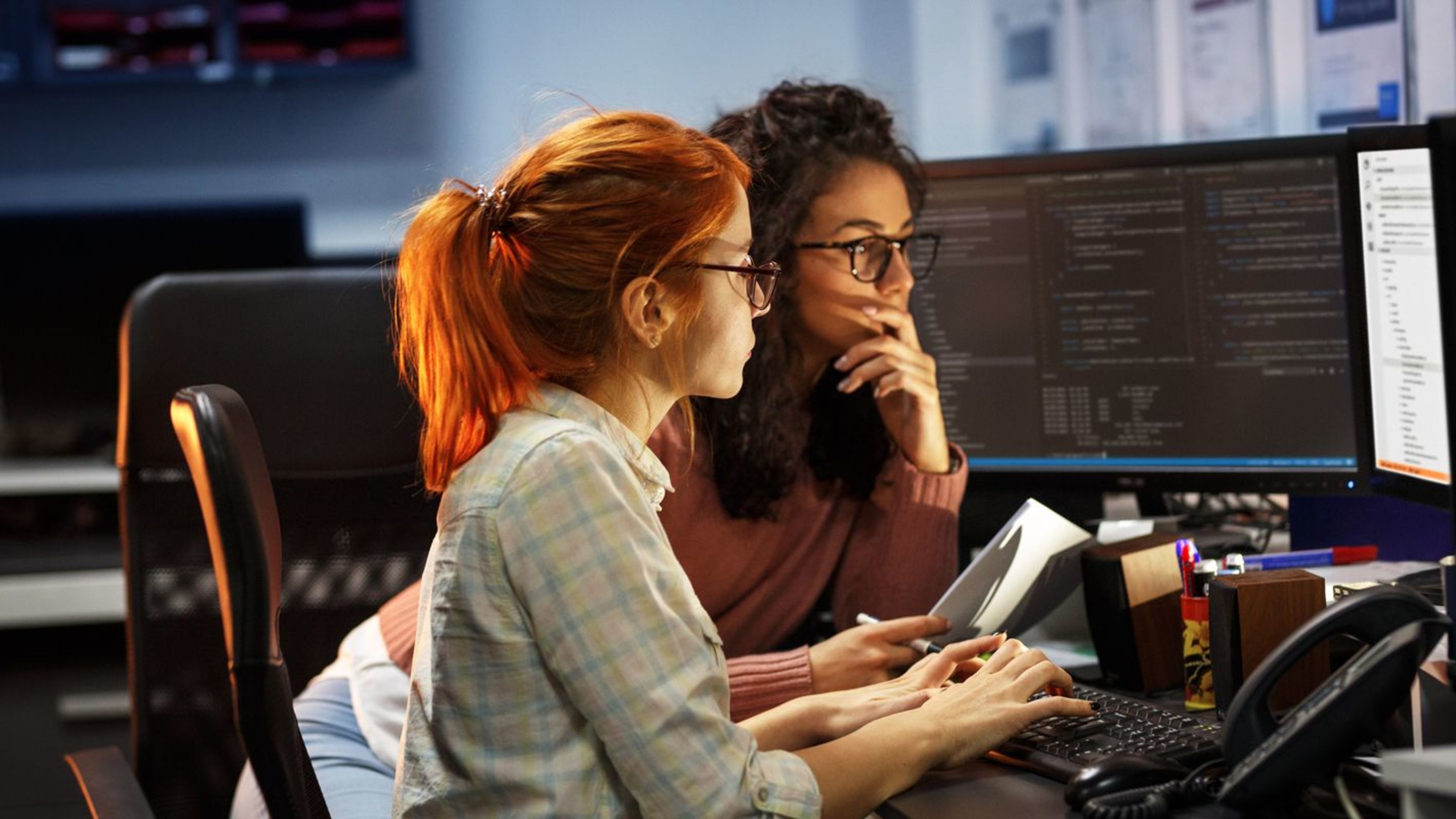 Two female programmers examining code on a desktop.  